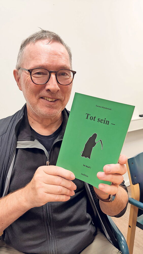 Mann mit grünem Buch 'Tot sein' in der Hand Mann hält ein grünes Buch mit dem Titel 'Tot sein'.