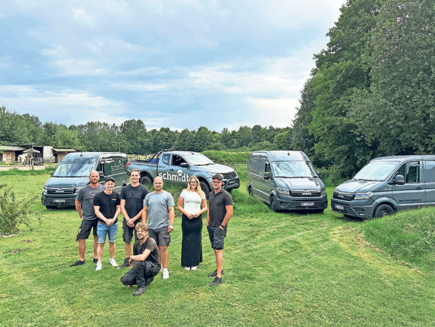 Teamfoto auf einer grünen Wiese Gruppe posiert auf Wiese vor drei grauen Fahrzeugen.
