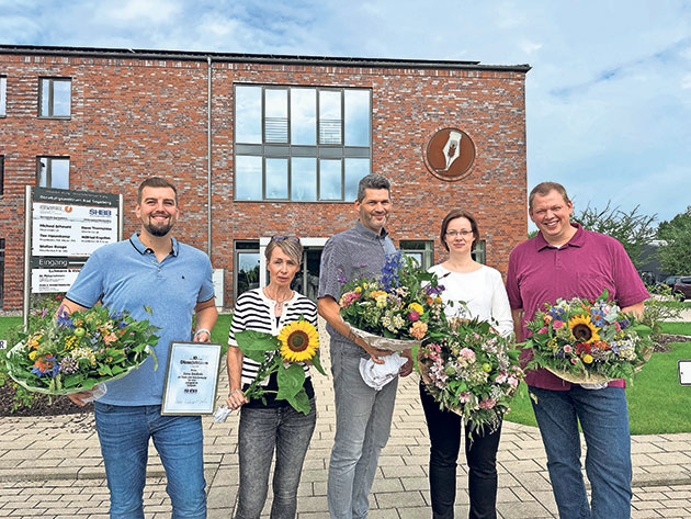 Personen mit Blumen vor Backsteingebäude in Sommerkleidung Gruppe von fünf Personen mit Blumensträußen vor einem Backsteingebäude.
