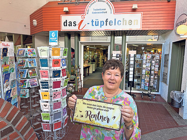 Geschäftseingang mit Grußkarten und Frau mit Schild. Frau hält Schild vor Geschäft mit Grußkarten.