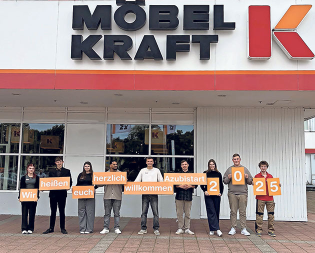 Azubis vor Möbel Kraft mit Willkommensschildern.