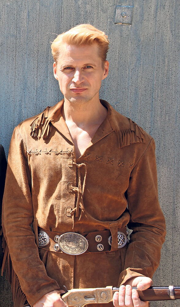 Cowboy-Kleidung vor grauer Wand Mann in brauner Cowboy-Kleidung vor einer Wand.