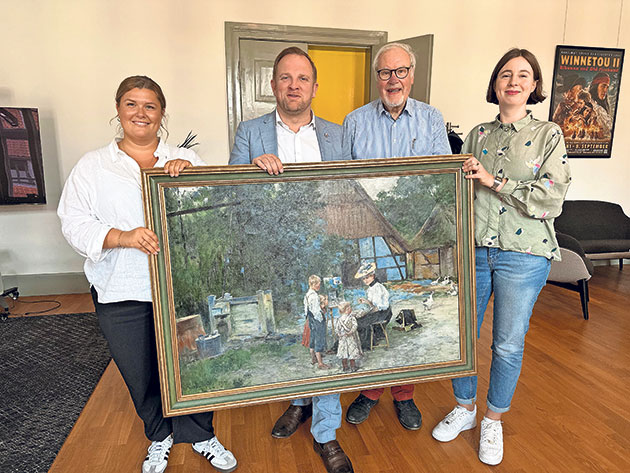 Personen präsentieren Kunstwerk in einem Raum. Vier Personen halten gemeinsam ein großes Gemälde.