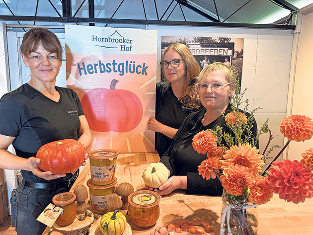 Herbstglück am Hornbrooker Hof Drei Frauen präsentieren Kürbisprodukte auf einem Herbstmarkt.