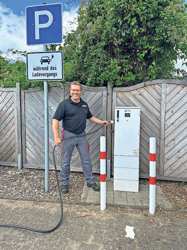 Mann an Ladesäule auf Parkplatz Mann steht neben Ladesäule mit Parkschildern im Hintergrund.