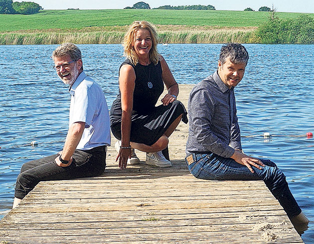 Gruppenbild auf einem Steg am Wasser Drei Menschen sitzen auf einem Steg am See.