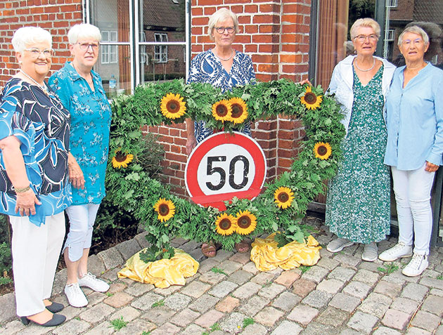 Jubiläum mit Blumen und Verkehrsschild Fünf Frauen stehen mit Sonnenblumen umrahmter 50.