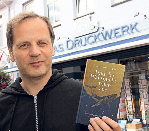 Buchvorstellung vor 'Das Druckwerk' Mann hält Buch vor Buchhandlung 'Das Druckwerk'.