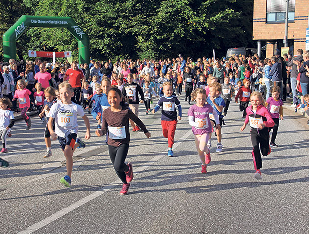 Kinderlauf beginnt unter einem grünen Startbogen. Kinder starten bei einem Laufwettbewerb auf einer Straße.