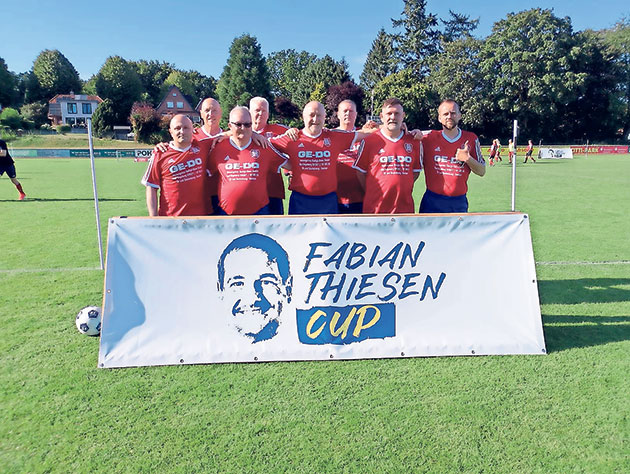 Gruppe von Fußballspielern hinter einem Banner auf dem Rasen.