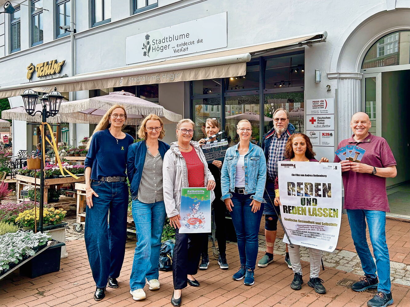 Menschen versammeln sich mit Plakaten vor Stadtblume Höger. Gruppe von Menschen vor einem Blumenladen mit Plakaten.