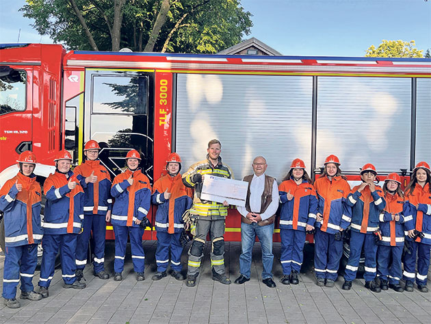 Gruppe vor Feuerwehrauto hält einen Scheck