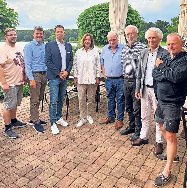 Acht Personen stehen draußen in einer Reihe. Gruppe von acht Personen posiert im Freien auf einer Terrasse.