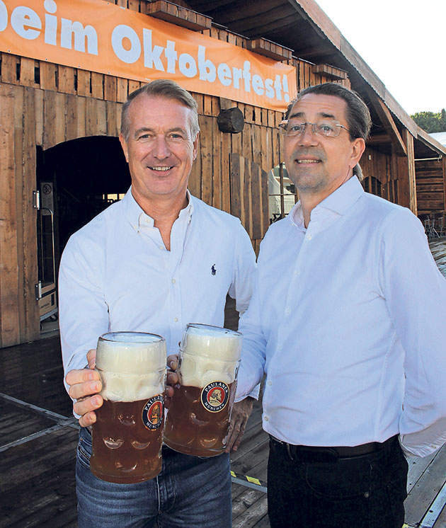 Zwei Männer mit Bierkrügen vor Oktoberfest-Dekor.