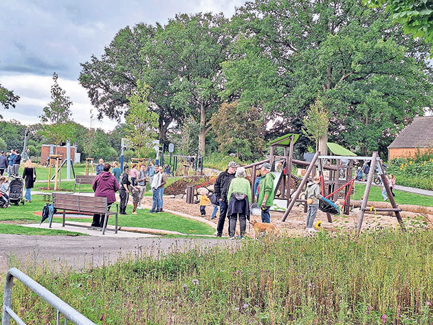 Spielplatz voller Kinder und Erwachsener im Grünen. Kinder spielen auf einem Spielplatz, Erwachsene schauen zu.