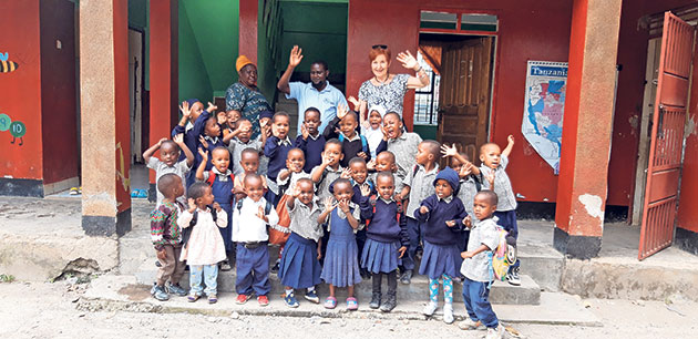 Fröhliche Gruppe vor Schule in Tansania. Kinder und Erwachsene winken vor einem Gebäude.