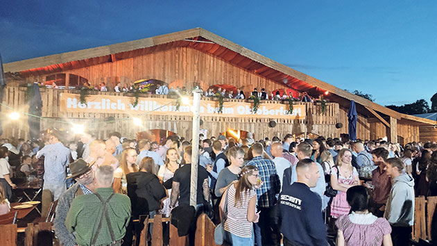 Feiernde Menschen beim Oktoberfest-Abend Menschenmenge vor einem Holzgebäude beim Oktoberfest.