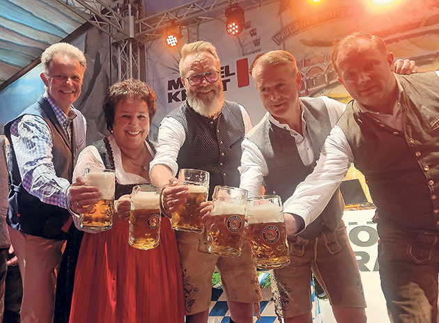 Fünf Personen heben Bierkrüge in einem Festzelt.