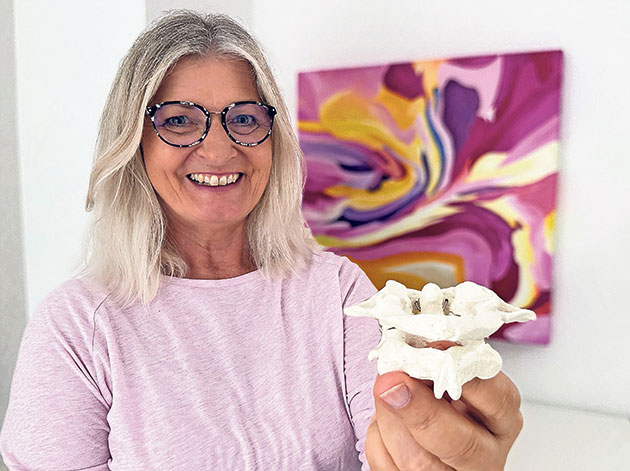 Frau hält ein Knochenmodell vor einem farbigen Bild.