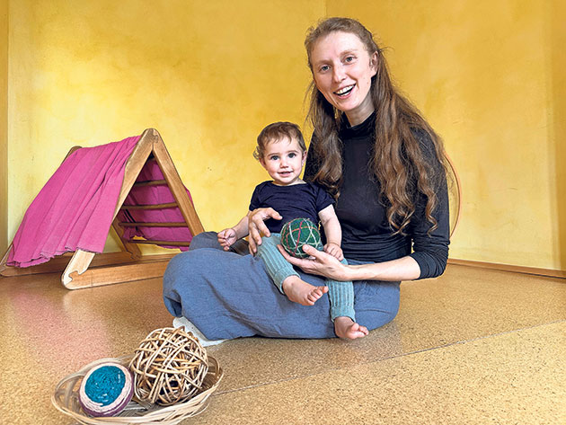 Frau mit kleinem Kind spielt mit Bällen auf dem Boden.