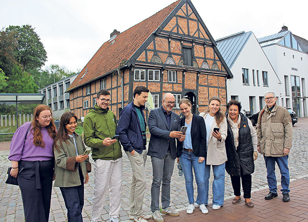 Gruppe steht lächelnd vor einem Fachwerkhaus und schaut auf Handys.