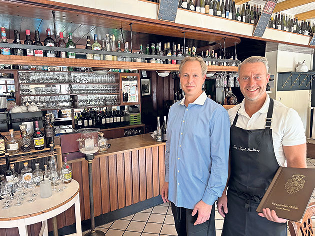 Männer stehen lächelnd vor einer gut bestückten Bar. Zwei Männer vor einer Bar mit Getränken.