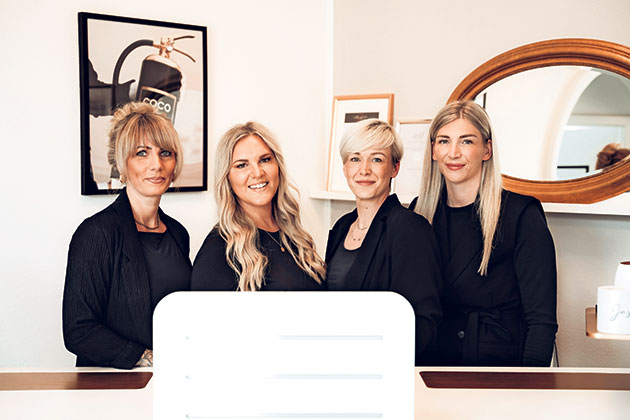 Vier Frauen stehen lächelnd hinter einem Empfangstresen.