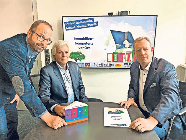Werbebesprechung zur Immobilienkompetenz Drei Männer an einem Tisch vor Immobilien-Werbung.