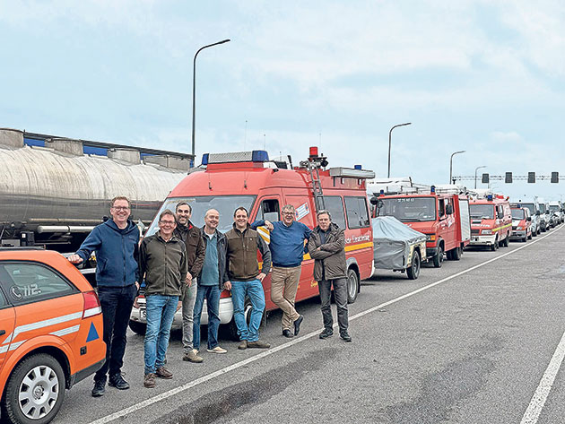 Männer stehen vor Feuerwehrfahrzeugen auf einer Straße.