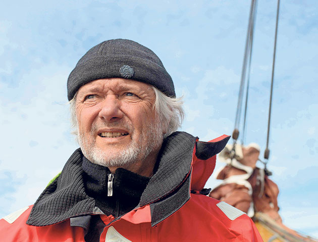 Mann in roter Jacke auf einem Boot, mit blauem Himmel.