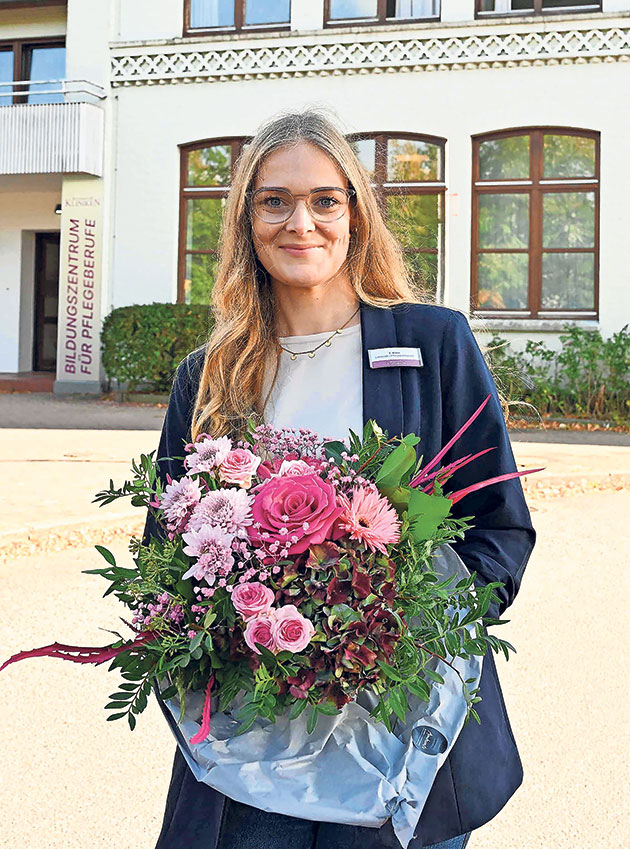 Frau mit Blumenstrauß vor einem Gebäude lächelt in die Kamera.