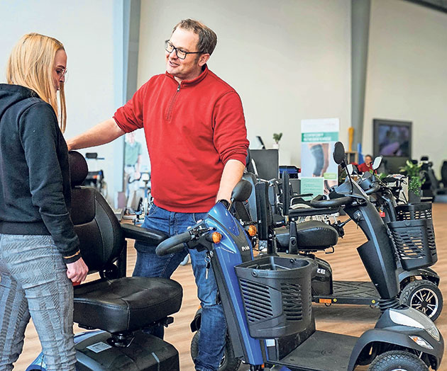 Mann zeigt Frau einen Mobilitätsscooter im Geschäft.