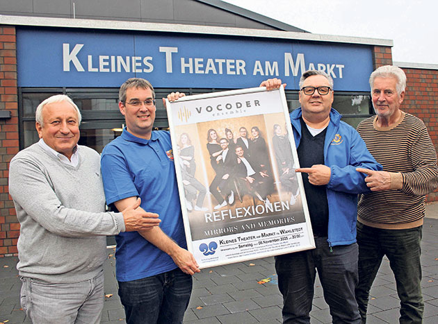 Vier Männer halten ein Konzertplakat vor einem kleinen Theater.