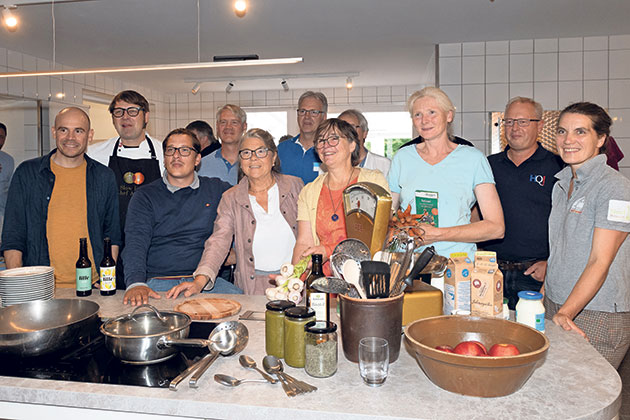 Gruppe von Menschen in einer Küche, Kochutensilien auf dem Tisch.