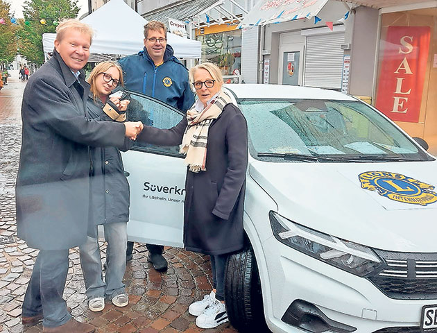 Lions-Club veranstaltet Autoübergabe in der Stadt. Gruppe posiert mit Auto bei Lions-Club-Event in der Stadt.