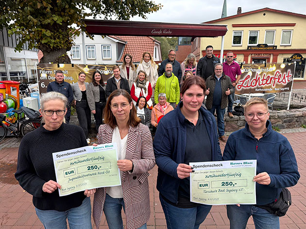Gruppenbild mit Scheckübergabe bei einem Stadtfest. Gruppe mit Spendenschecks vor einem Zeltfest.