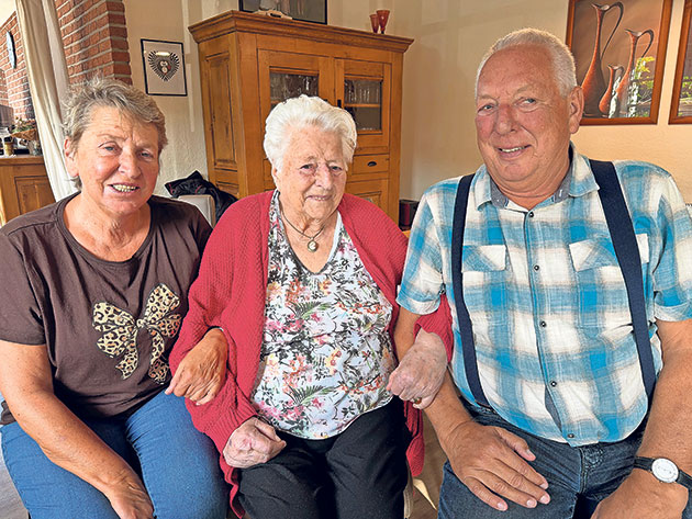Älteres Trio auf Sofa in gemütlicher Atmosphäre Drei ältere Personen sitzen lächelnd auf einem Sofa.