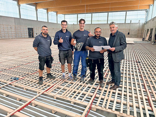 Gruppenfoto auf Baustelle mit Holzboden Team auf Baustelle mit Holzbodenaufbau und Plänen