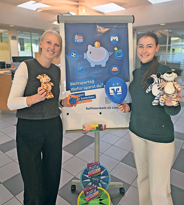 Weltspartag: Frauen präsentieren Poster und Spielzeug Zwei Frauen mit Spielzeug vor einem Weltspartag-Poster.