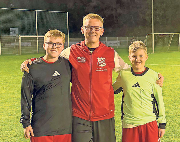 Freunde auf dem Fußballplatz bei Nacht Drei Personen stehen auf einem Fußballplatz und lächeln.