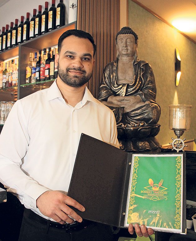 Mann zeigt Speisekarte in einem Restaurant mit Buddha-Statue.