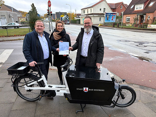 Übergabe des Lastenrads in Bad Segeberg Drei Personen mit Lastenrad vor Straßenszene.