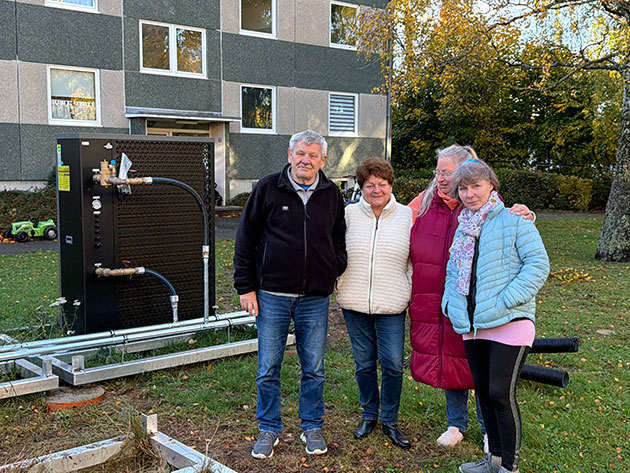 Vier Menschen vor einem Gebäude mit Wärmepumpe im Freien.