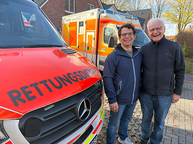 Zwei Männer vor Rettungswagen und Gebäude.
