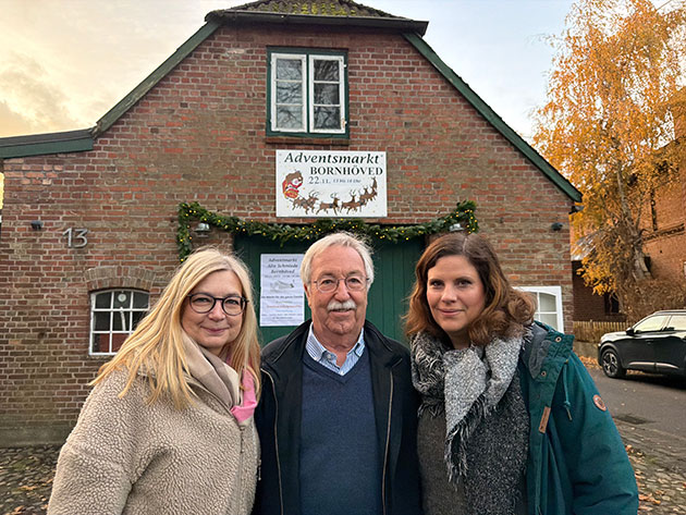 Drei Personen vor einem Haus mit Adventsmarkt-Schild.