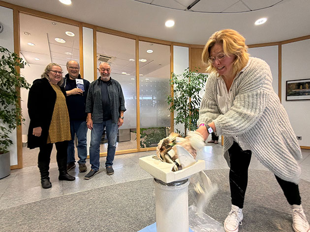 Frau zerschlägt symbolisch Porzellan vor drei Beobachtern im Büro.
