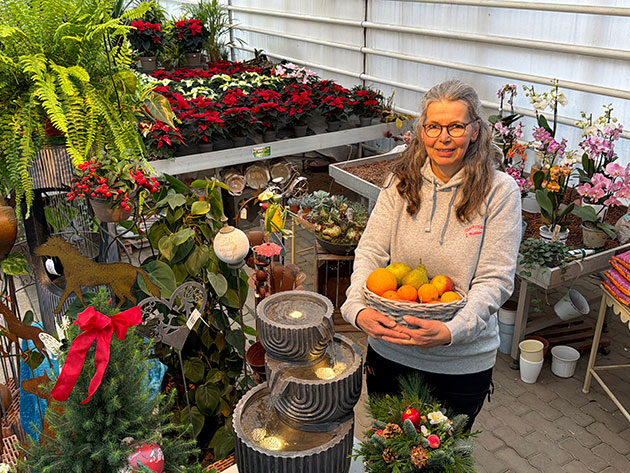 Frau im Gewächshaus hält Korb mit Früchten.