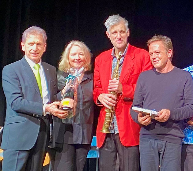 Gruppe von vier Personen posiert mit Geschenken auf einer Bühne.