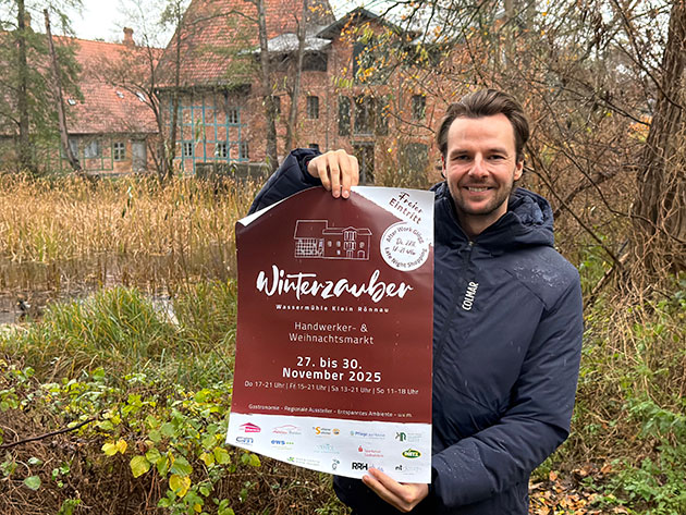 Mann hält Plakat für Winterzauber-Markt in der Hand.