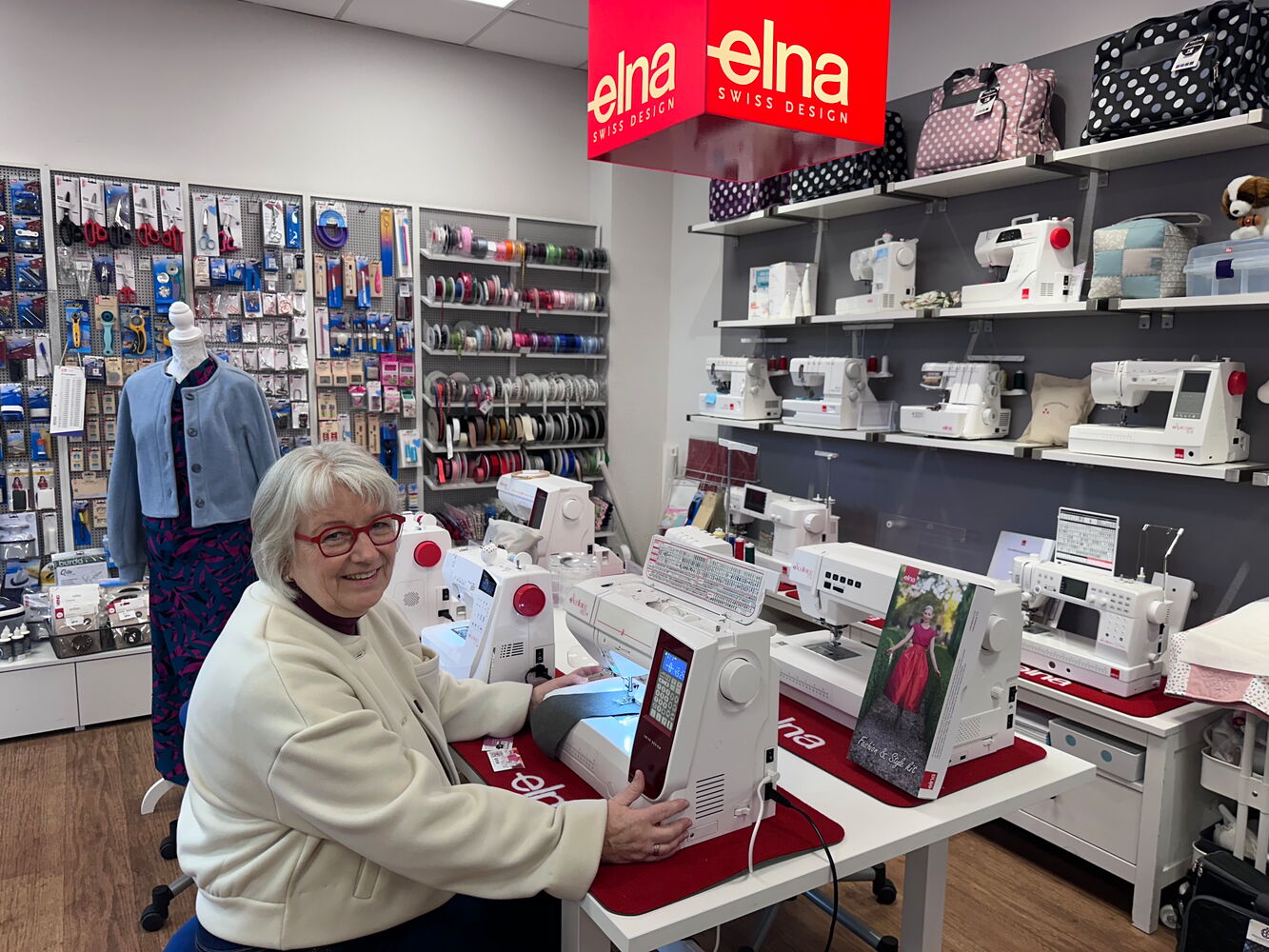 Frau sitzt an Nähmaschine in einem Geschäft voller Zubehör.